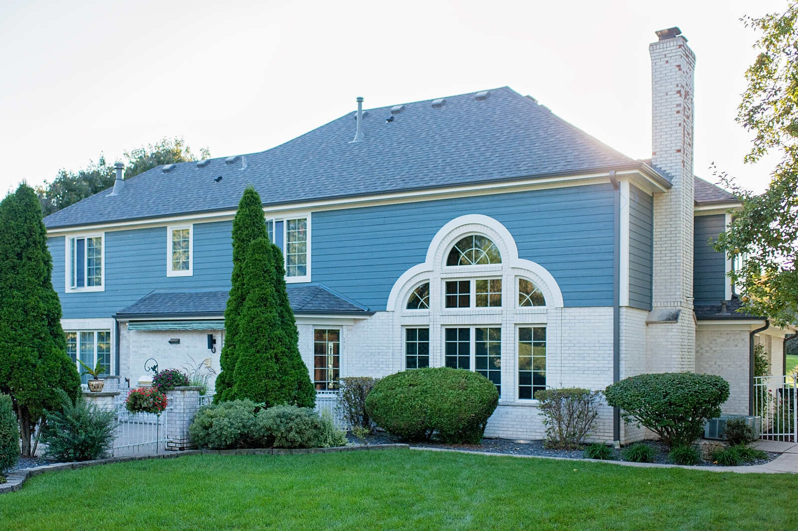 A rear view of a blue house with large windows and a spacious backyard by Smardbuild in Naperville, Chicago